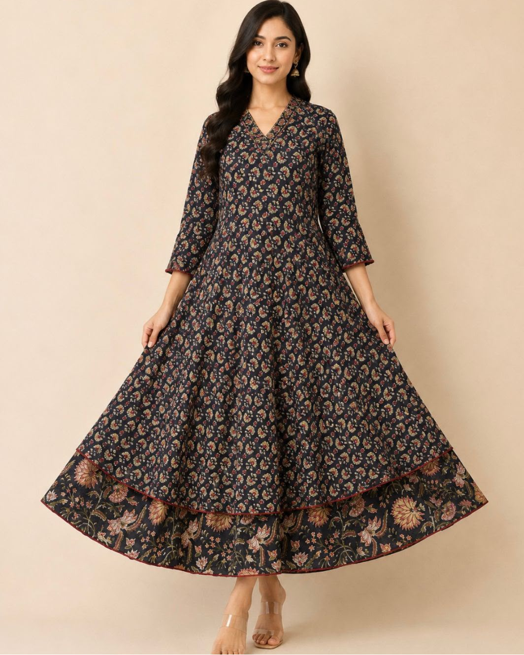 A woman modeling a long-sleeved, V-neck maxi dress with a dark navy blue base and an all-over beige and brown floral print, set against a solid beige studio background.