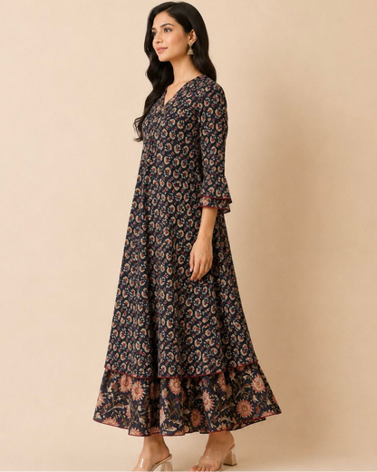 A woman modeling a long-sleeved, V-neck maxi dress with a dark navy blue base and an all-over beige and muted orange floral pattern, set against a solid beige studio background.