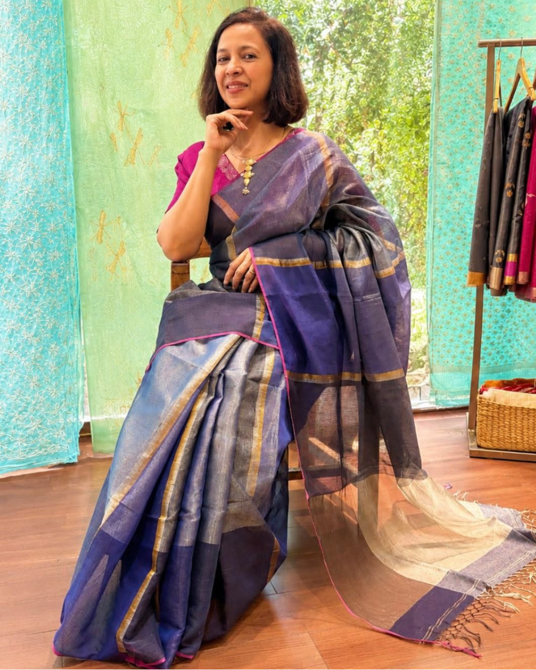 Woman in a blue saree sitting on a wooden floor with a colorful background