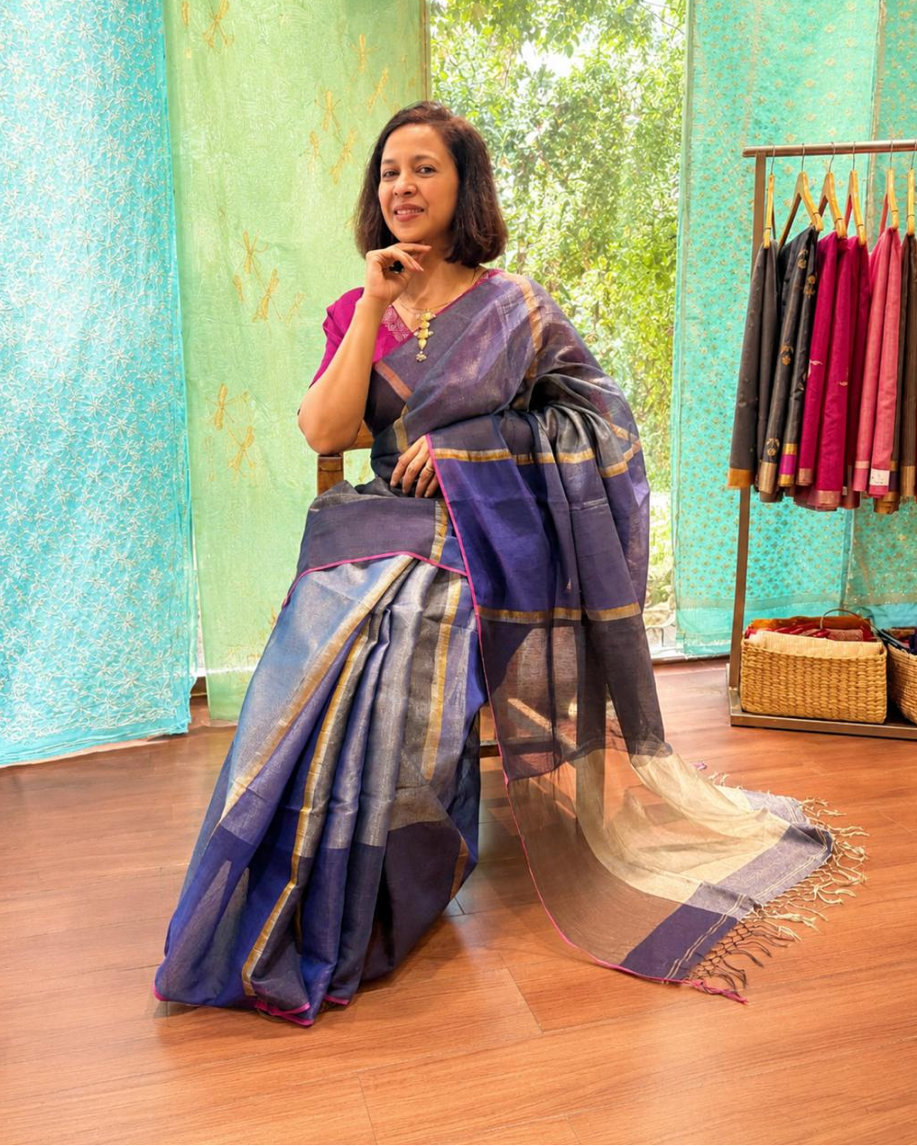 Woman in a blue and purple saree standing in a store with colorful sarees in the background.