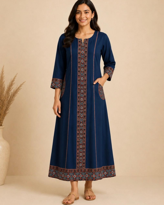 A woman modeling a long navy blue kurta with intricate geometric and floral patterns in brown, red, and white along the center placket, cuffs, and hem, set against a warm beige background.