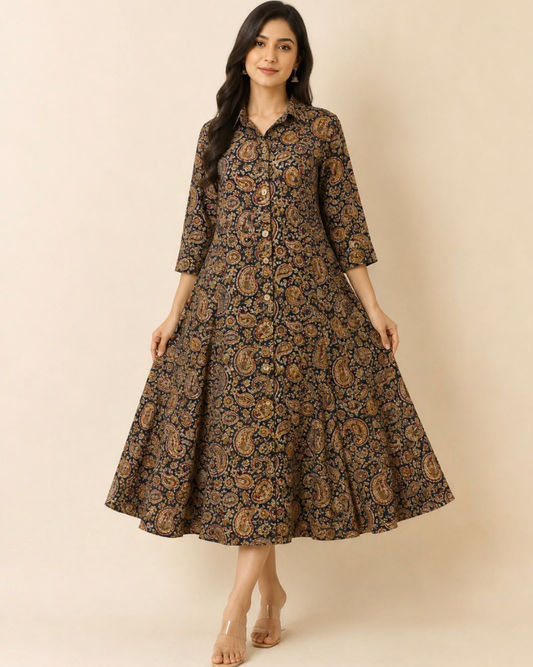A woman modeling a long-sleeved, button-front midi dress with a flared skirt. The dress features an all-over intricate paisley and floral block print in brown, gold, and black.