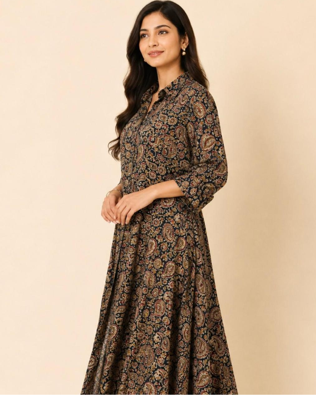 A woman modeling a long-sleeved, button-up maxi dress with a dark brown and black paisley pattern, set against a solid beige studio background.
