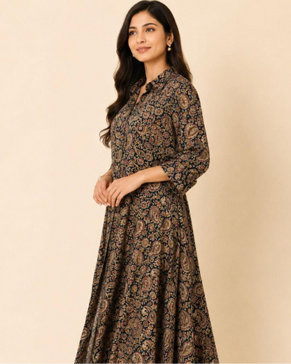 A woman modeling a long-sleeved, button-up maxi dress with a dark brown and black paisley pattern, set against a solid beige studio background.