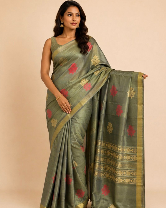A woman modeling a sage green silk saree with red floral motifs and gold zari borders, posed against a solid beige studio background.