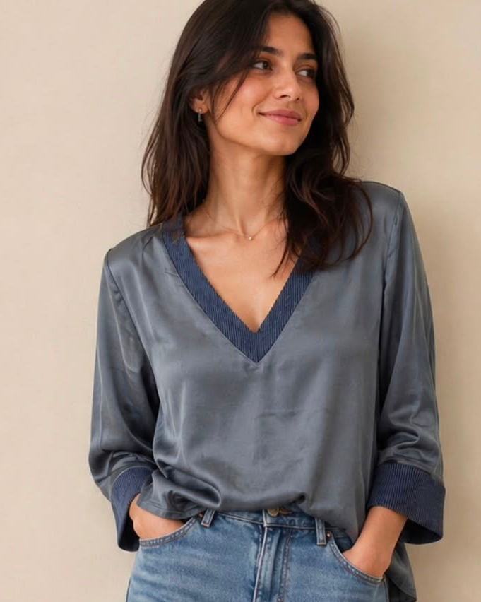 Woman wearing a gray blouse and blue jeans against a beige background