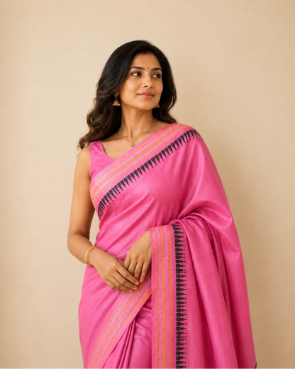 A woman modeling a bright pink silk saree with a black and orange geometric border, paired with a matching pink sleeveless blouse, set against a solid beige background.