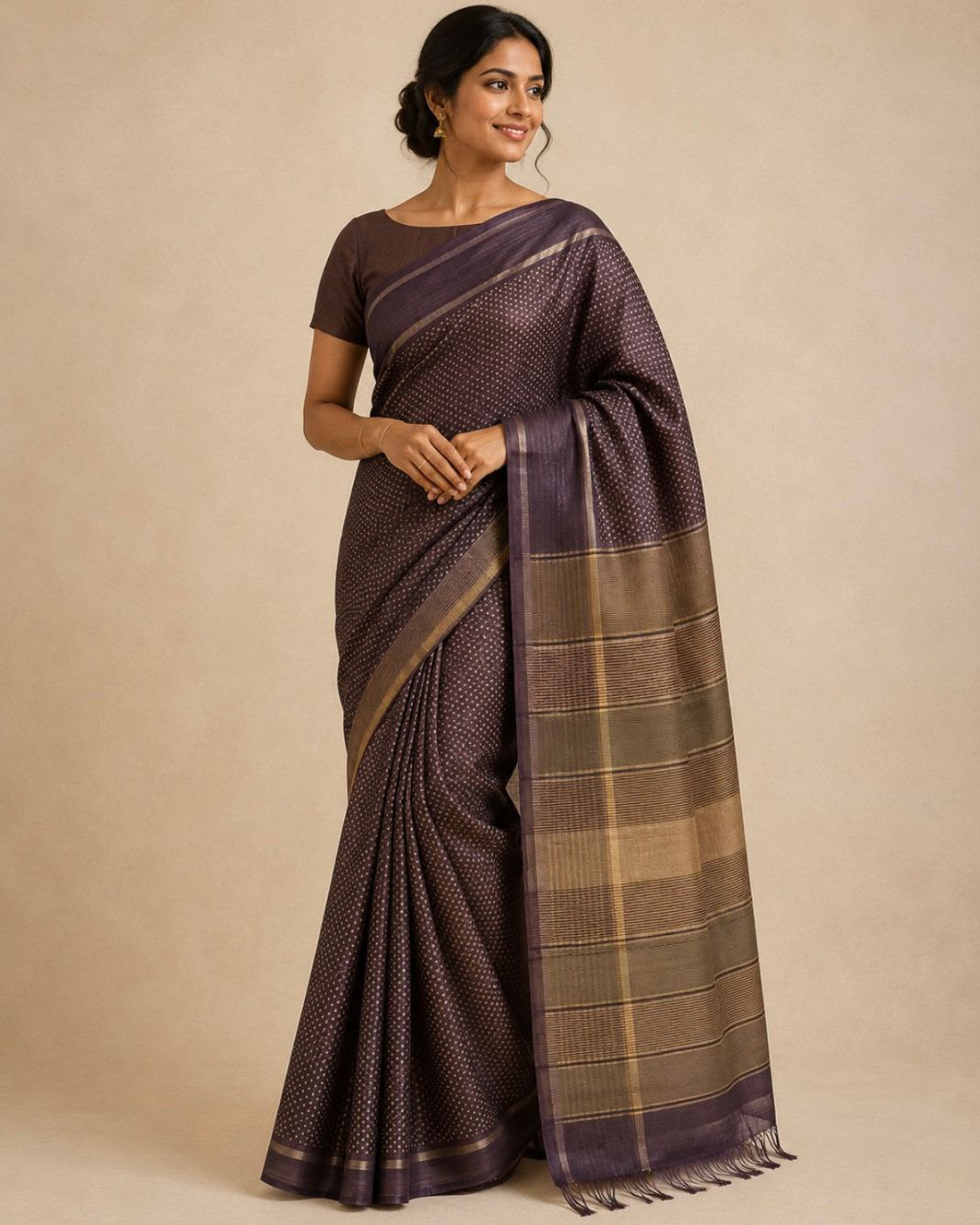 A woman modeling a dark purple and brown patterned saree with a matching short-sleeve blouse against a plain beige studio background.