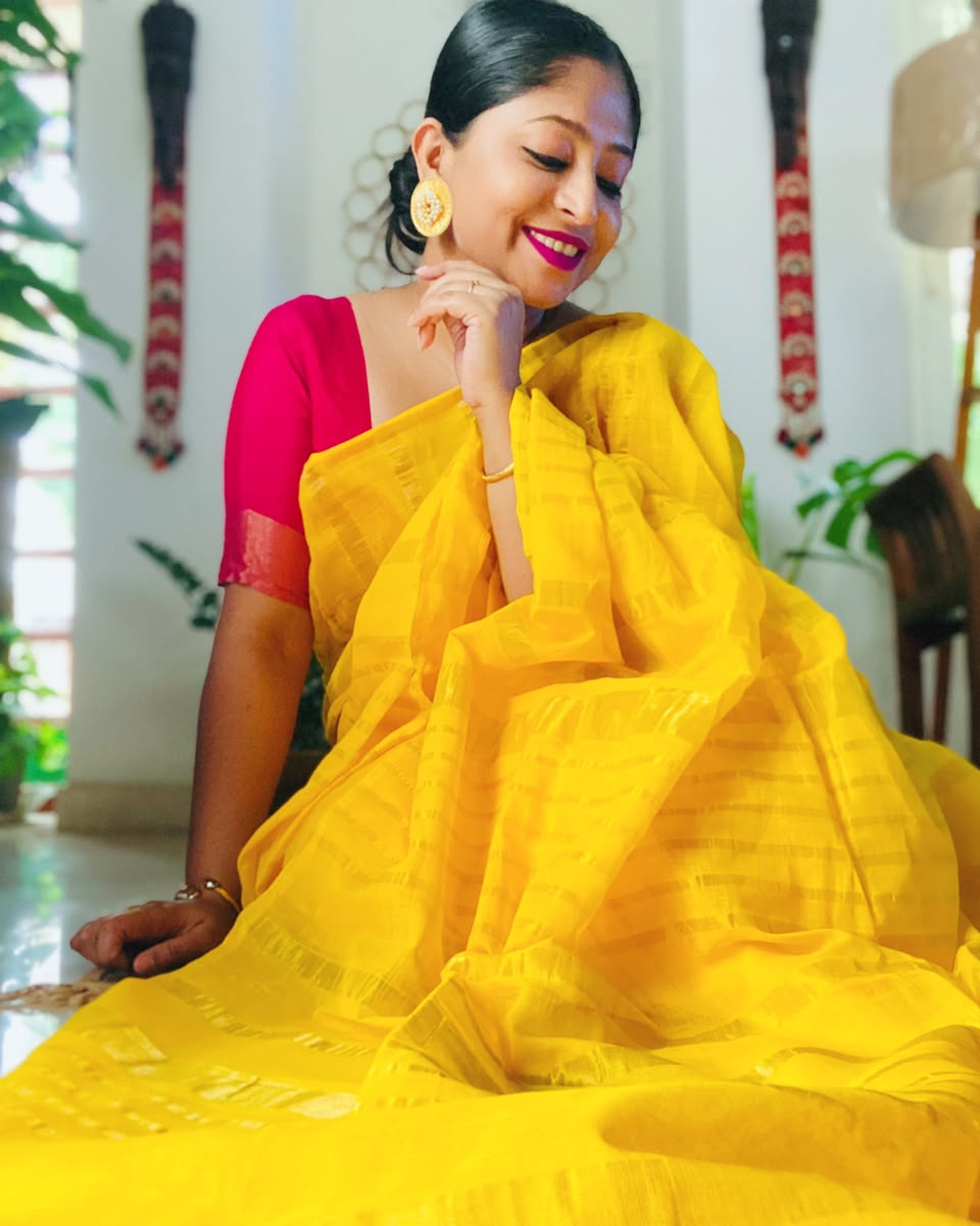 Woman wearing a yellow saree with a red blouse indoors.
