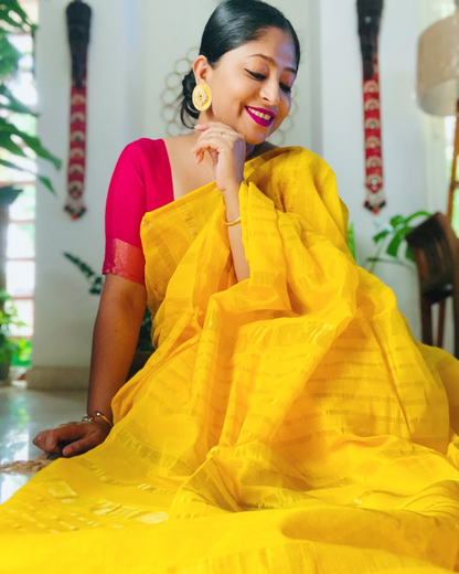Woman wearing a yellow saree with a red blouse indoors.